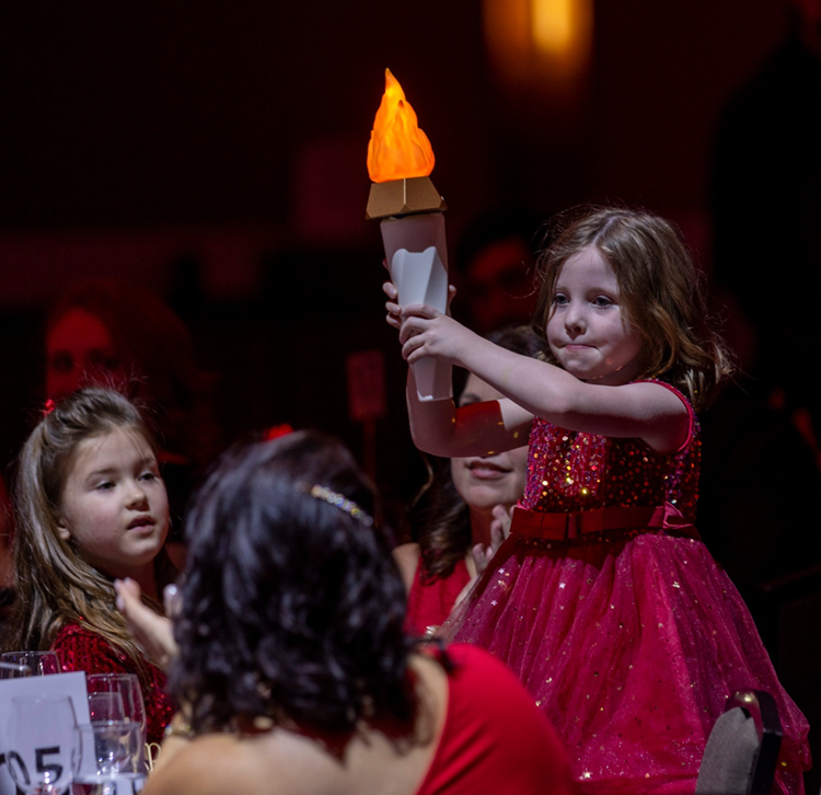 Little girl in red dress holding up a torch.
